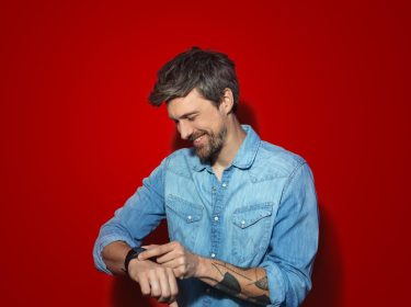 Samsung Galaxy Watch LTE: Mann vor rotem Hintergrund schaut lachend auf seine Smartwatch