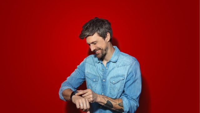 Samsung Galaxy Watch LTE: Mann vor rotem Hintergrund schaut lachend auf seine Smartwatch