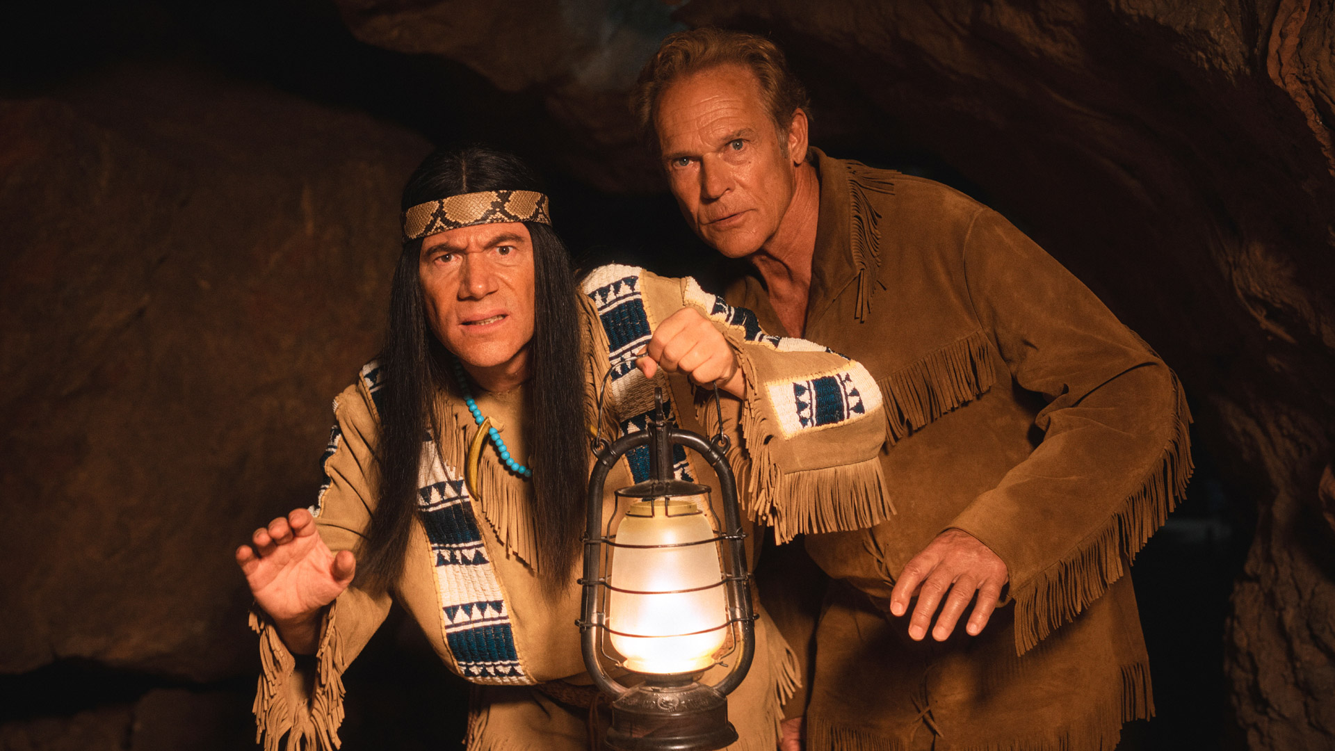 Auf diesem Bild zur Das Kanu des Manitu Kritik schleichen Michael Bully Herbig als Abahachi und Christian Tramitz als Ranger durch eine dunkle Höhle. Abahachi hält eine leuchtende Petroleumlampe vor sich, beide schauen aufmerksam und leicht angespannt nach vorn. Die Szene wirkt geheimnisvoll und spannungsgeladen.