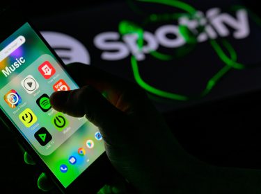 Hand tippt auf das App-Symbol für Spotify auf einem Handy.