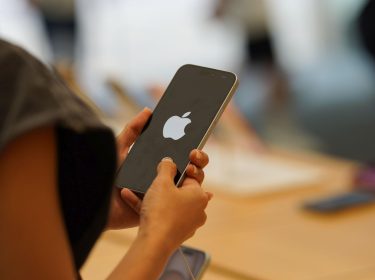 Frau hält iPhone in den Händen, auf dessen Display das Apple-Logo zu sehen ist.