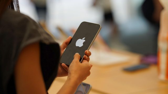 Frau hält iPhone in den Händen, auf dessen Display das Apple-Logo zu sehen ist.