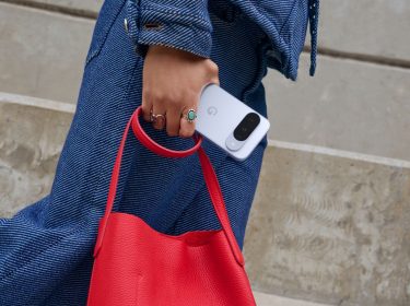 Eine Person hält das Pixel 10 und eine rote Handtasche in der Hand.
