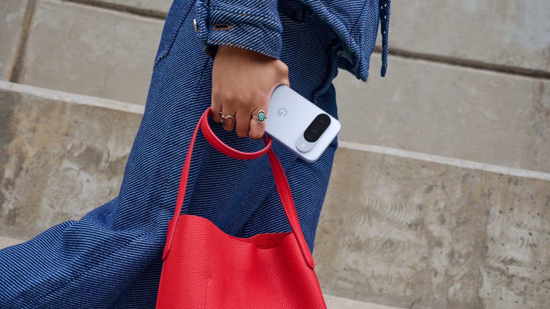 Eine Person hält das Pixel 10 und eine rote Handtasche in der Hand.