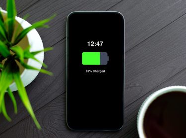 Im Artikel iphone-Akku tauschen zeigt dieses Bild ein modernes iPhone mit schwarzem Display auf einem dunklen Holztisch. Der Bildschirm zeigt 82 Prozent Akkuladung.