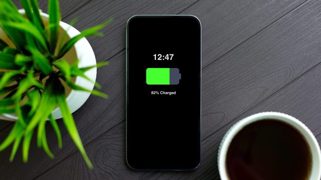 Im Artikel iphone-Akku tauschen zeigt dieses Bild ein modernes iPhone mit schwarzem Display auf einem dunklen Holztisch. Der Bildschirm zeigt 82 Prozent Akkuladung.