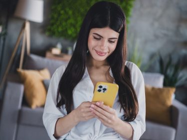 Junge Frau schaut auf ein iPhone mit gelber Hülle.