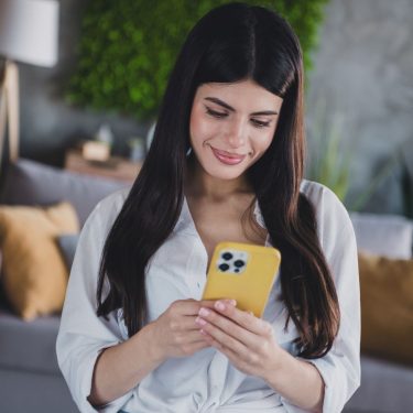 Junge Frau schaut auf ein iPhone mit gelber Hülle.