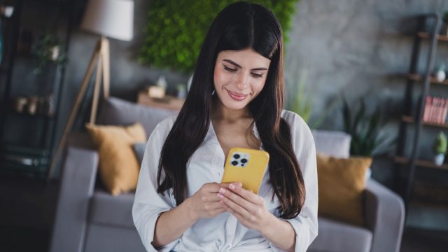 Junge Frau schaut auf ein iPhone mit gelber Hülle.