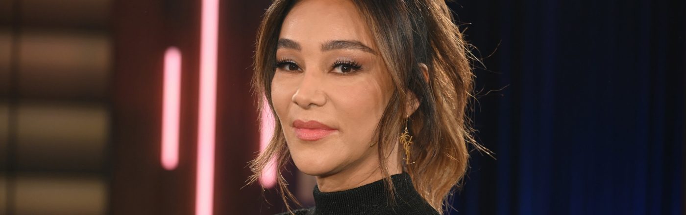 Dieses Symbolbild zu Villa der Versuchung 2026 zeigt Moderatorin Verona Pooth in einem schwarzen, hochgeschlossenen Oberteil mit feinem Muster. Sie steht vor einem Studiolicht-Hintergrund mit dunklen Blau- und Rosatönen. Ihr Blick ist ruhig und selbstbewusst, das Bild vermittelt eine elegante und professionelle Stimmung.