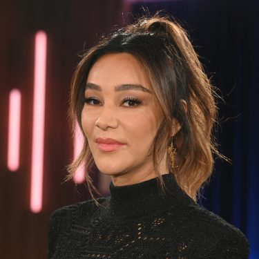 Dieses Symbolbild zu Villa der Versuchung 2026 zeigt Moderatorin Verona Pooth in einem schwarzen, hochgeschlossenen Oberteil mit feinem Muster. Sie steht vor einem Studiolicht-Hintergrund mit dunklen Blau- und Rosatönen. Ihr Blick ist ruhig und selbstbewusst, das Bild vermittelt eine elegante und professionelle Stimmung.