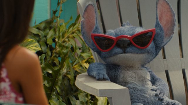 Stitch sitzt auf einem Holzstuhl und trägt eine Sonnenbrille.