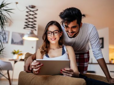 Ein junges Paar schaut gemeinsam auf ein Tablet und lächelt dabei.