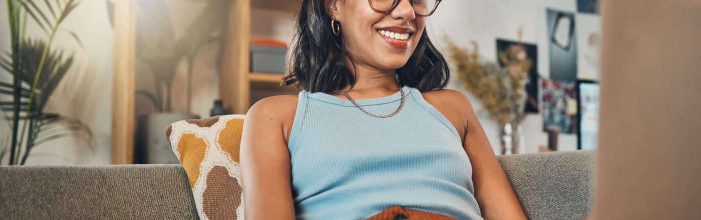 Eine Frau sitzt mit einem Laptop auf dem Schoß auf einer Couch.