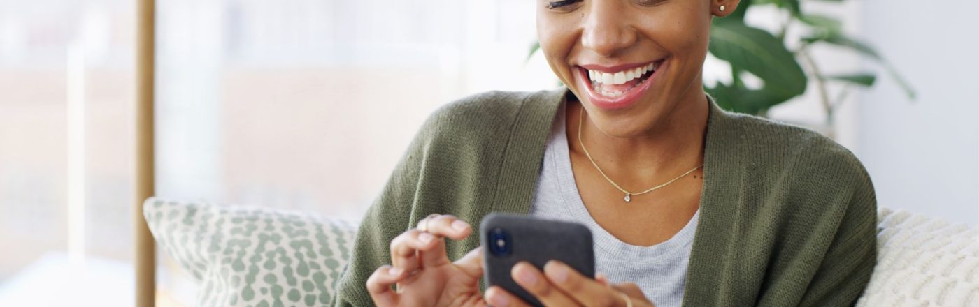 Junge Schwarze Frau schaut lächelnd auf ihr Android-Handy.