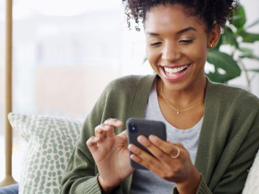 Junge Schwarze Frau schaut lächelnd auf ihr Android-Handy.