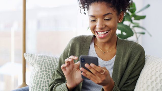 Junge Schwarze Frau schaut lächelnd auf ihr Android-Handy.