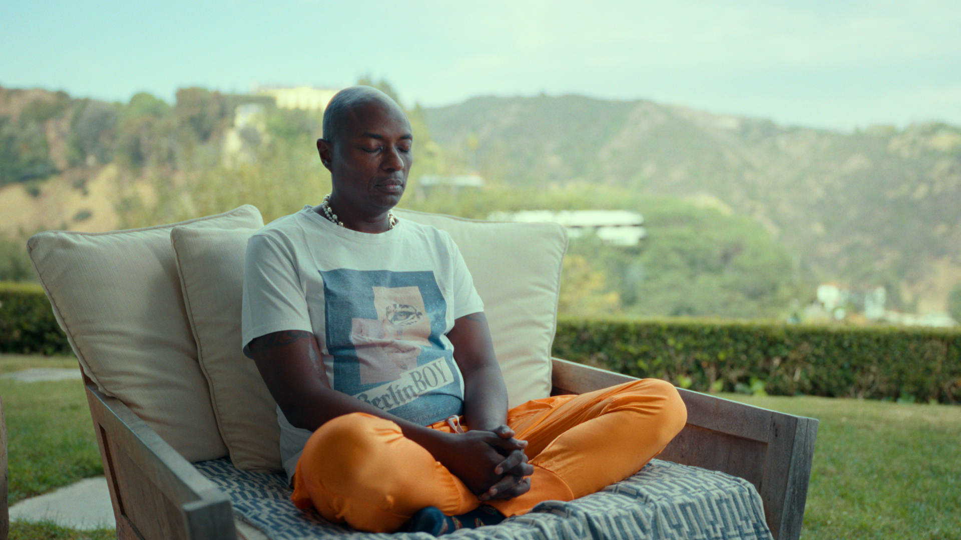 Durek Verrett sitzt im Schneideseit auf einem breiten Sessel im Freien und hat die Augen geschlossen.