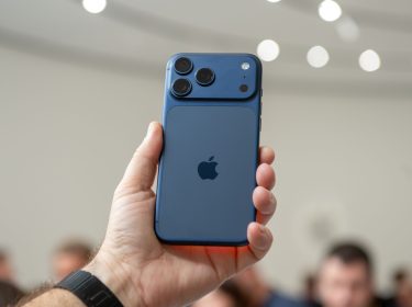 Hand hält das iPhone 17 Pro in Blau in die Höhe, im Hintergrund sind unscharf Menschen zu erkennen