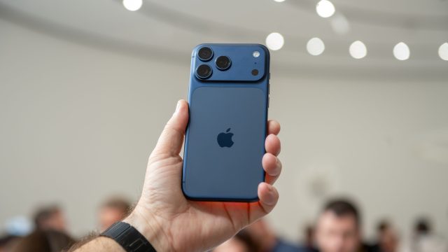 Hand hält das iPhone 17 Pro in Blau in die Höhe, im Hintergrund sind unscharf Menschen zu erkennen