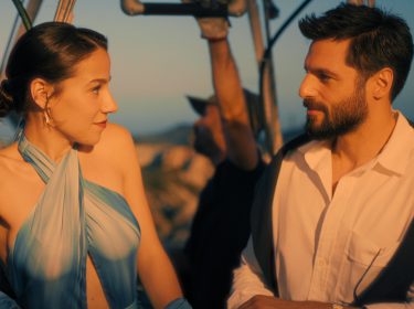 Szenenbild aus dem Netflix-Film She Said Maybe: Eine elegant gekleidete Frau und ein gut aussehender Mann mit Bart blicken sich an.