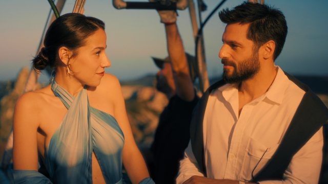 Szenenbild aus dem Netflix-Film She Said Maybe: Eine elegant gekleidete Frau und ein gut aussehender Mann mit Bart blicken sich an.