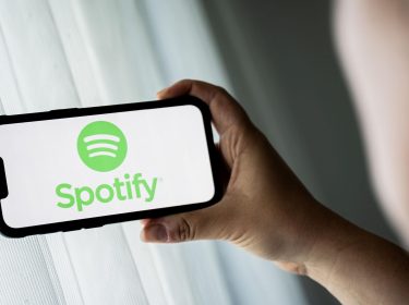 Mann schaut auf iPhone-Display, auf dem das Logo von Spotify abgebildet ist.