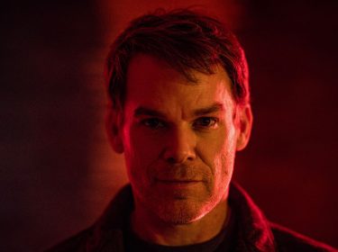 Auf dem Bild zu Dexter: Wiedererwachen ist Dexter Morgan zu sehen, gespielt von Michael C. Hall. Er blickt ernst und direkt in die Kamera, umgeben von dramatischem Rotlicht, das eine düstere und spannungsgeladene Stimmung erzeugt. Das Bild vermittelt eine intensive Atmosphäre, passend zur düsteren Serie.