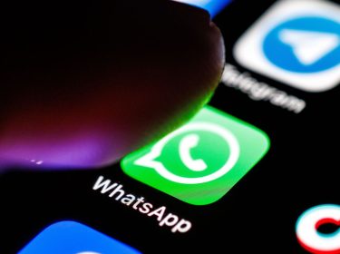Das WhatsApp-Logo ist auf dem Display eines Smartphones zu sehen, während sich ein Zeigefinger dem App-Symbol nähert.