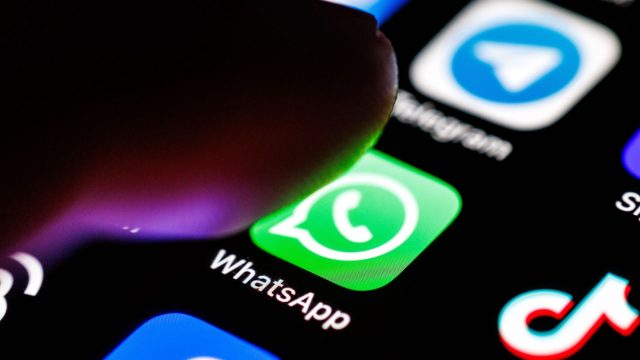 Das WhatsApp-Logo ist auf dem Display eines Smartphones zu sehen, während sich ein Zeigefinger dem App-Symbol nähert.