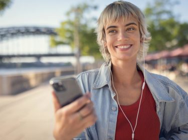 Datenverbauch Google Maps: Frau steht lächelnd mit ihrem Smartphone auf der Straße