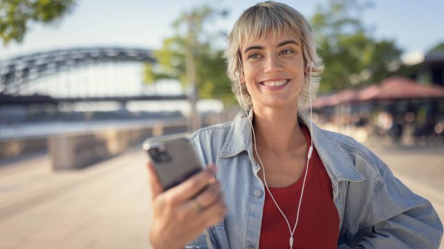 Datenverbauch Google Maps: Frau steht lächelnd mit ihrem Smartphone auf der Straße