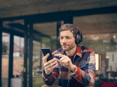 Datenverbrauch bei Videoanrufen: Mann sitzt mit Kopfhörern draußen und macht etwas an seinem Handy
