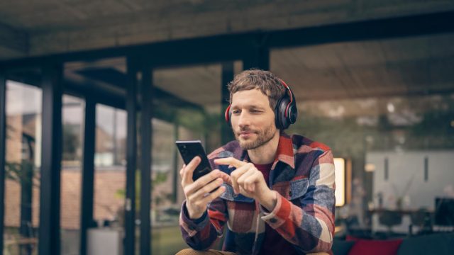 Datenverbrauch bei Videoanrufen: Mann sitzt mit Kopfhörern draußen und macht etwas an seinem Handy