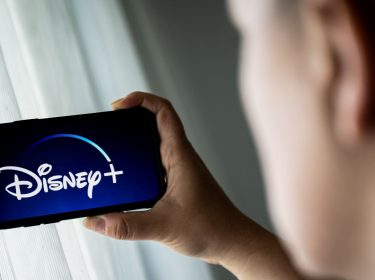 Mann schaut auf sein Smartphone, das das Logo von Disney+ zeigt.