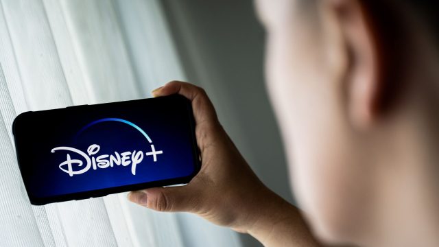 Mann schaut auf sein Smartphone, das das Logo von Disney+ zeigt.