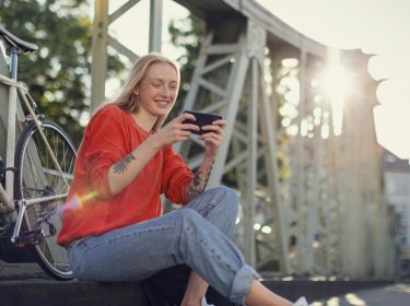 Roaming Xiaomi funktioniert nicht: junge Frau sitzt auf einer Brücke lächelnd neben ihrem Farrahd und schaut auf ihr Handy
