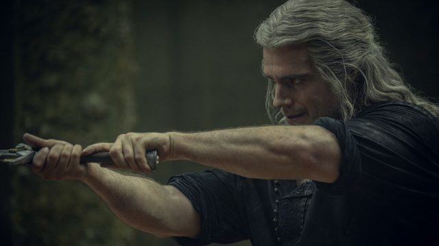 Schauspieler Henry Cavill in seiner Rolle als The Witcher hält mit beiden Händen ein Schwert