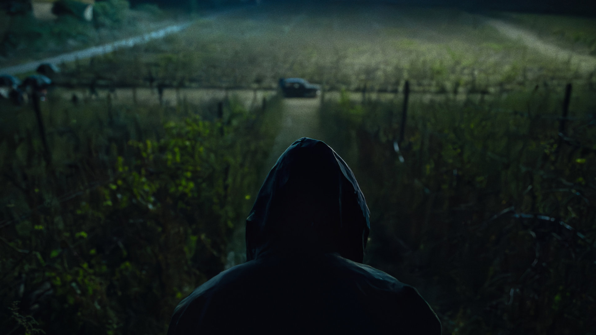 Ein Mann schaut auf der Ferne auf ein Auto, das nachts in der Feldmark parkt.