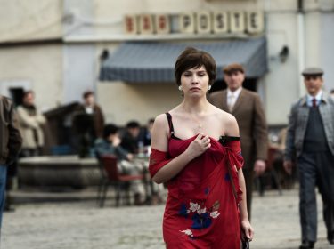 ein Frau in einem roten Kleid geht über einen Dorfplatz.