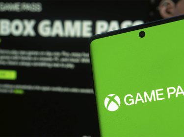 Ein Smartphone zeigt das Logo des Xbox Game Pass; im Hintergrund ist die geöffnete Game-Pass-App unscharf zu erkennen.