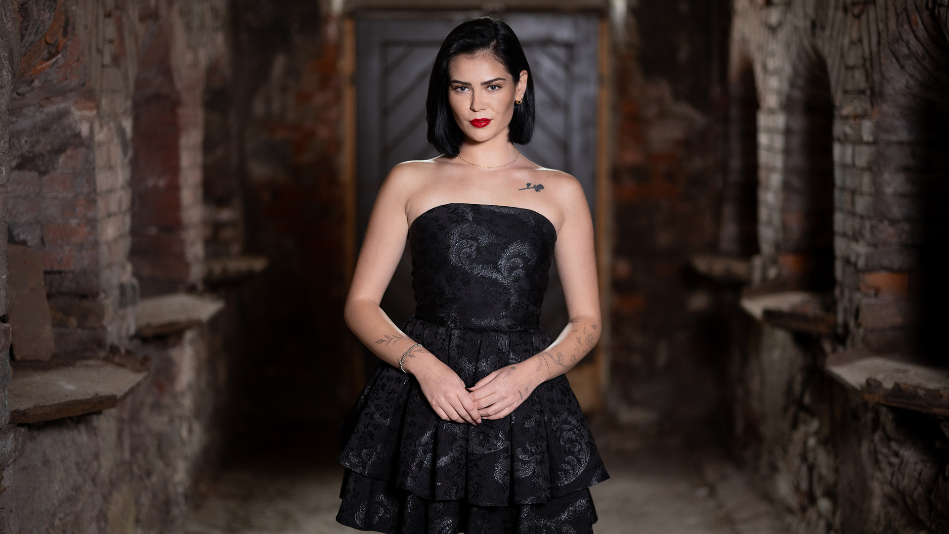 Linda Braunberger ist auf dem Bild zu „Das große Promi-Büßen“ 2025 in einem schwarzen trägerlosen Kleid mit floraler Struktur zu sehen.