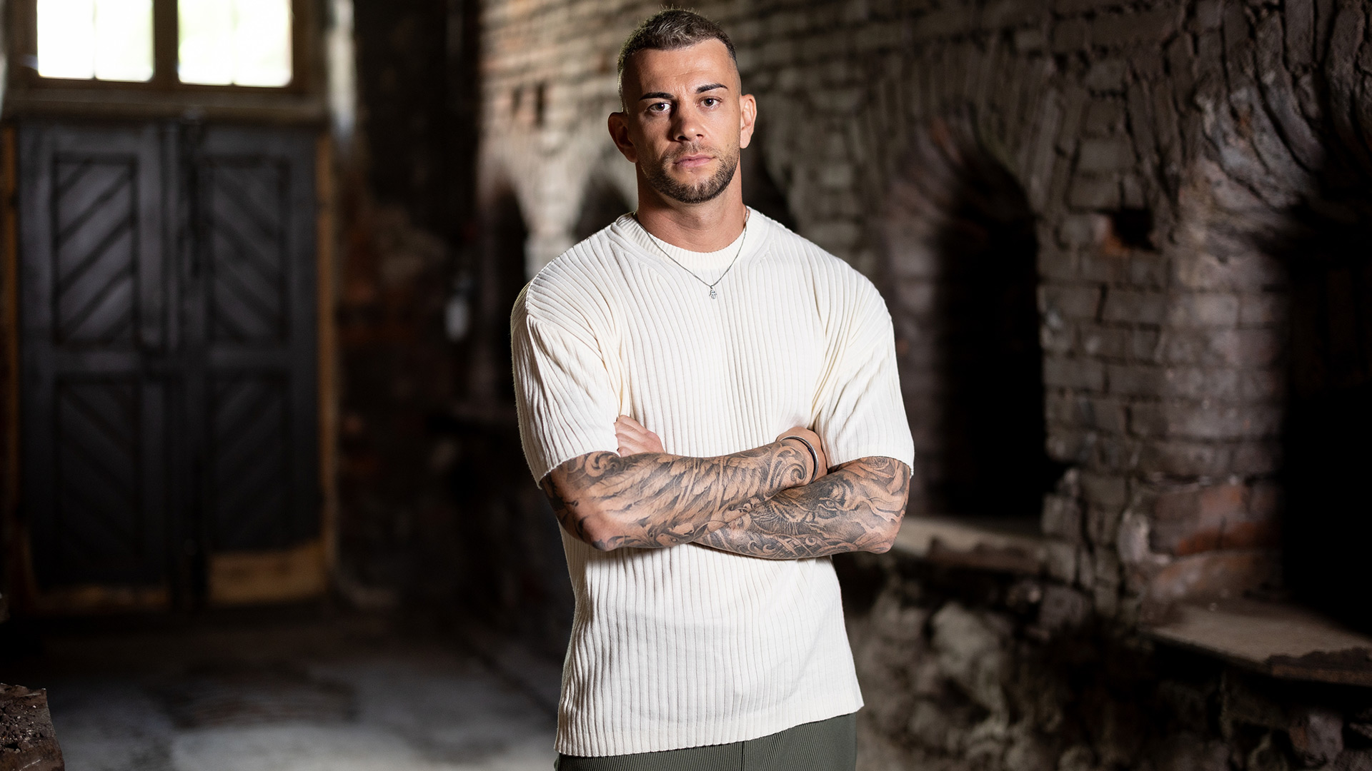 Serkan Yavuz steht auf dem Bild zu „Das große Promi-Büßen“ 2025 mit verschränkten Armen und ernstem Gesichtsausdruck.