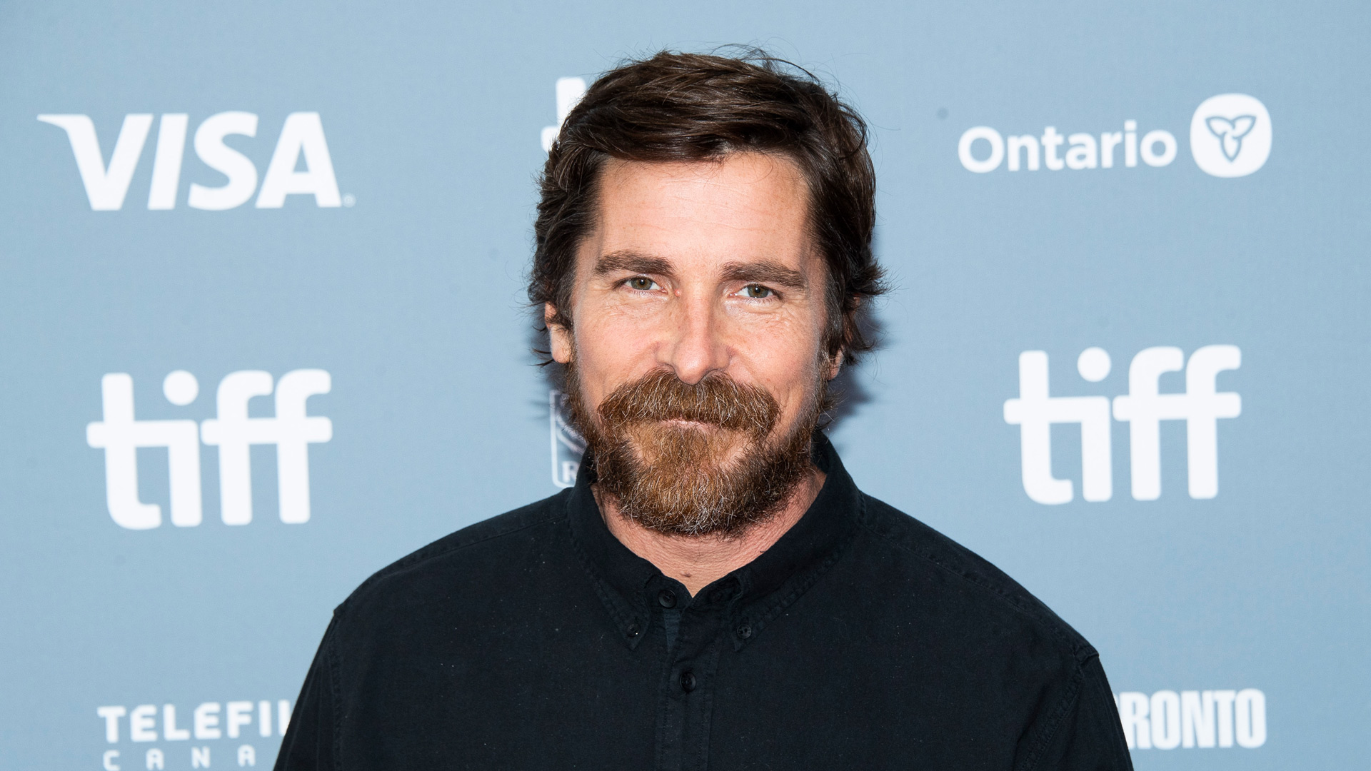 Christian Bale ist auf diesem Symbolbild bei einer Filmpremiere zu sehen. Er trägt ein schwarzes Hemd und blickt mit leichtem Lächeln in die Kamera. Der Schauspieler ist Teil des Casts von The Bride 2026 und spielt dort eine zentrale Rolle im düsteren Sci-Fi-Drama.