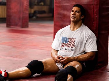 Dwayne Johnson in The Smashing Machine: Ein muskulöser Mann sitzt durchgeschwitzt und erschöpft auf dem Boden einer Trainingshalle.