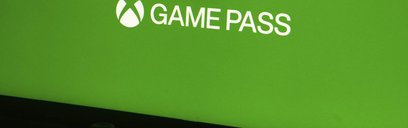 Ein Xbox-Controller liegt vor einem Monitor, der ein grünes Bild mit dem Game-Pass-Logo zeigt.