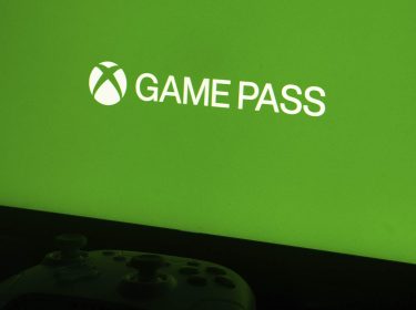 Ein Xbox-Controller liegt vor einem Monitor, der ein grünes Bild mit dem Game-Pass-Logo zeigt.