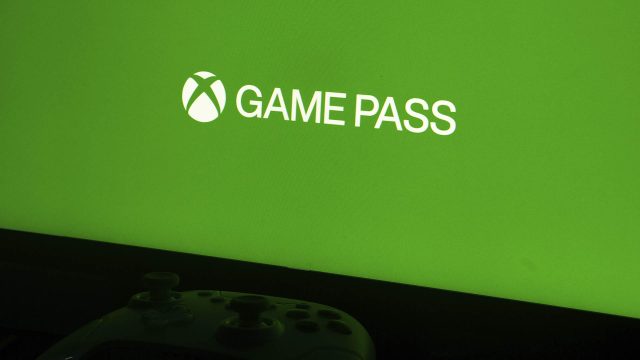 Ein Xbox-Controller liegt vor einem Monitor, der ein grünes Bild mit dem Game-Pass-Logo zeigt.
