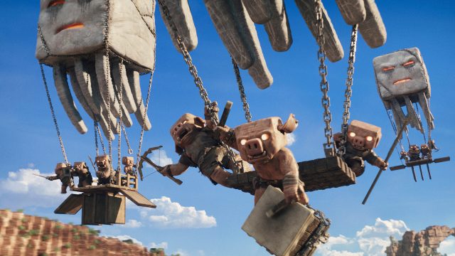 Auf dem Bild in dem Artikel zu „Ein Minecraft Film 2“ sind fliegende Kreaturen zu sehen, die hölzerne Plattformen mit mehreren Piglins durch die Luft tragen.