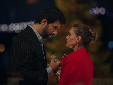 Engin Akyürek und Asli Enver in Altes Geld, neue Liebe: Ein adrett gekleideter Mann stößt mit einer Frau im roten Mantel mit tiefem Blick in die Augen an.